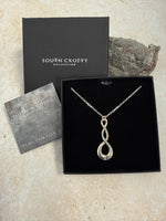 A Cornish tin pendant with a double twist design and a central sparkling diamond, presented on a 18-inch chain. In a black South Crofty presentation box with a certificate of authentication on a grey background.