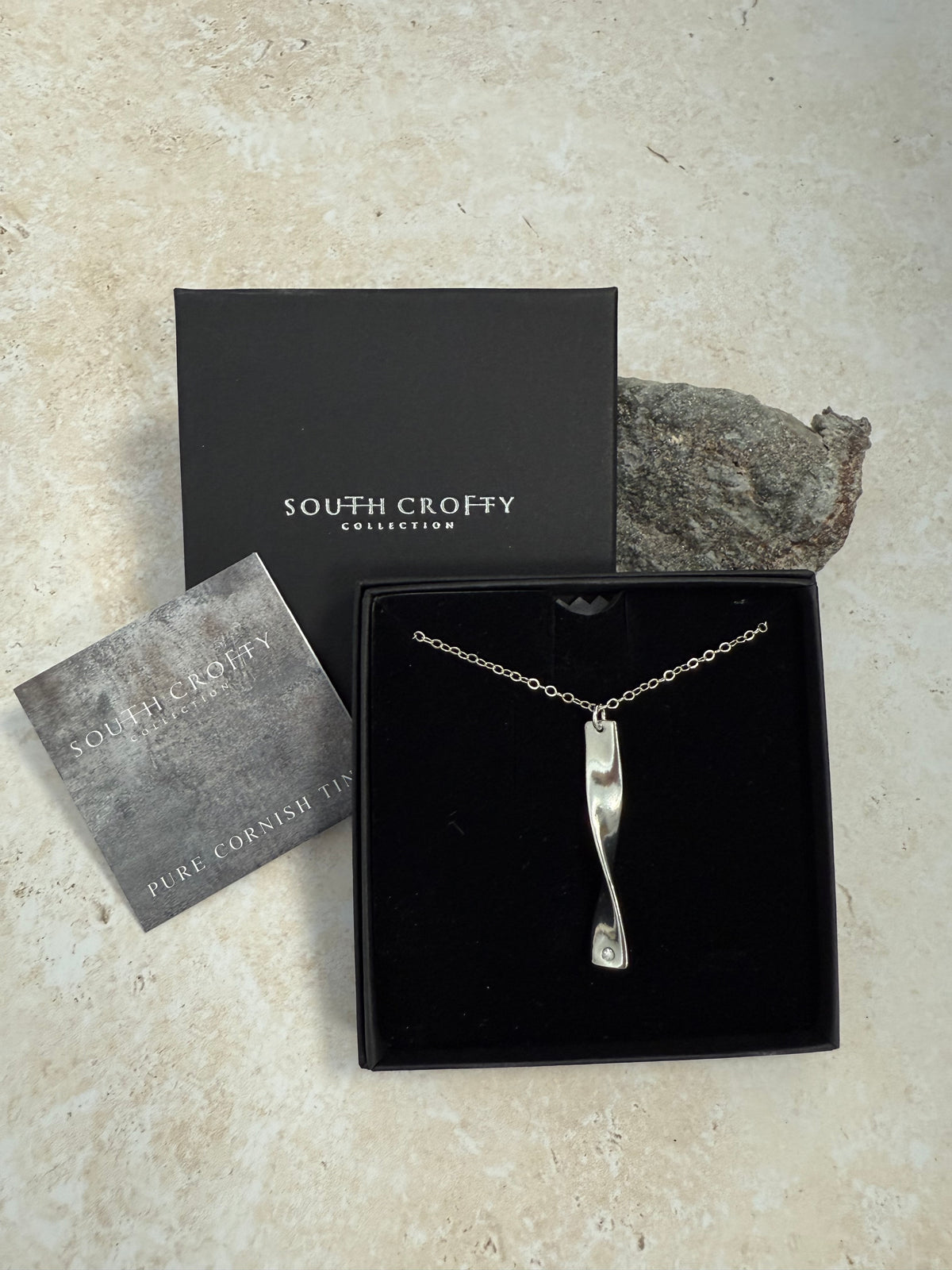 Cornish tin and diamond necklace in a South Crofty box on a textured surface. Next to a certificate of authenticity.
