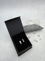 Black jewelry box with two Cornish tin stud earrings on a textured gray surface