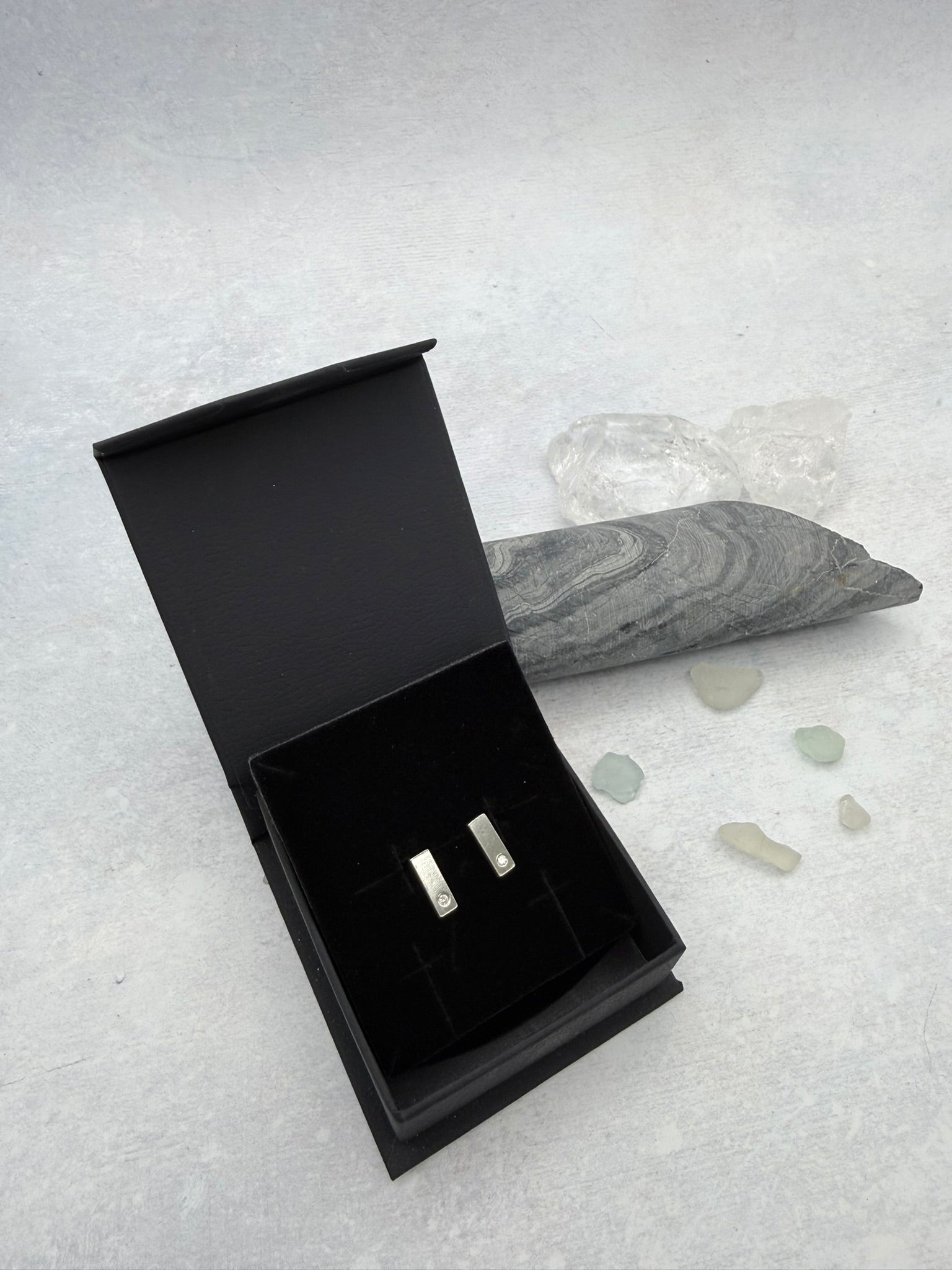 Black jewelry box with two Cornish tin stud earrings on a textured gray surface