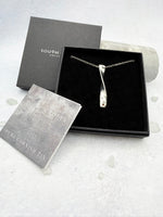 Cornish tin necklace which is silver in colour in a box with a certificate of authenticity for the tin on a light gray background