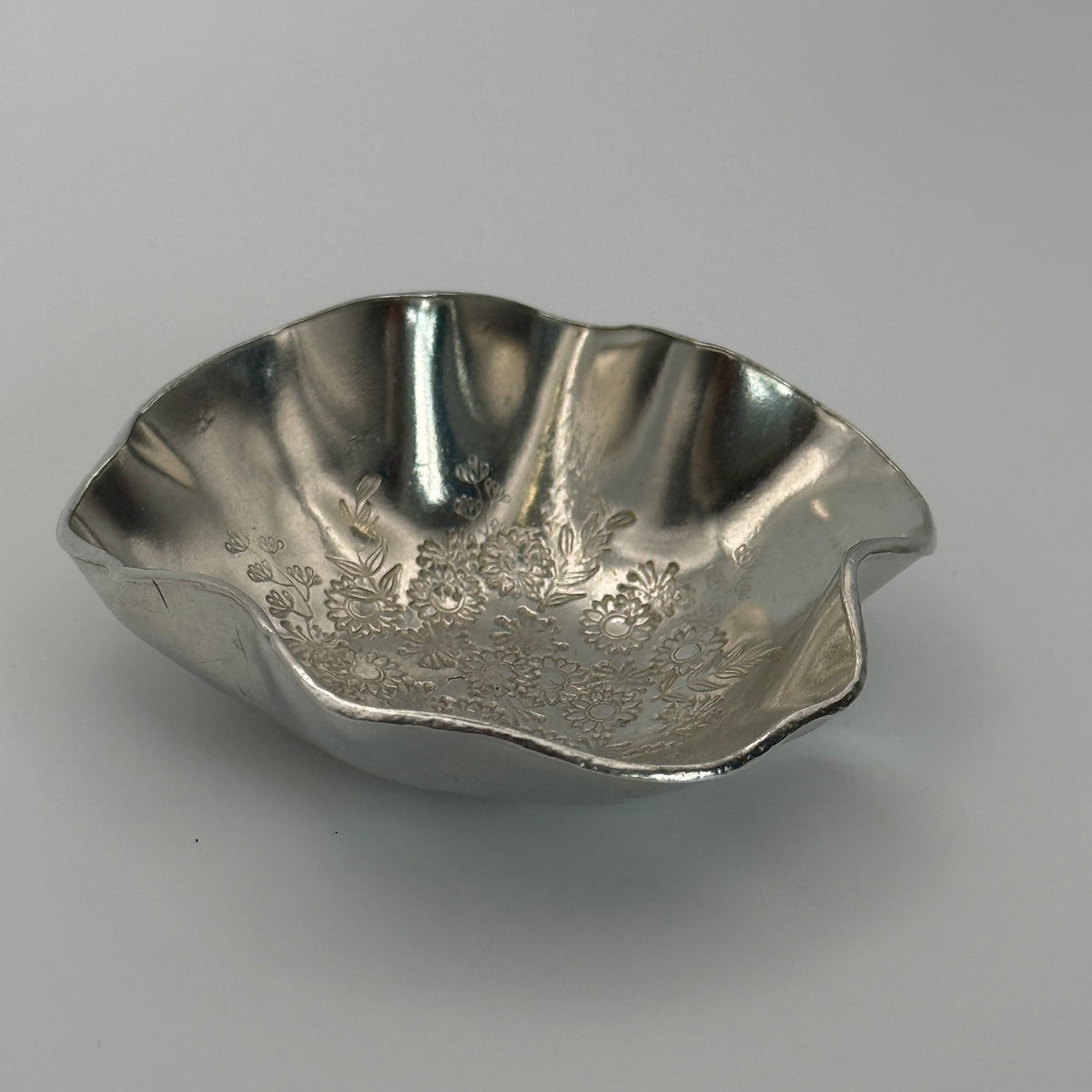 A trinket dish handmade from Cornish tin with waved edges and a hand stamped flower design in the base.