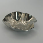 A trinket dish handmade from Cornish tin with waved edges and a hand stamped flower design in the base.