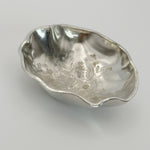 A trinket dish formed from Cornish tin with undulating edges and a stamped flower design