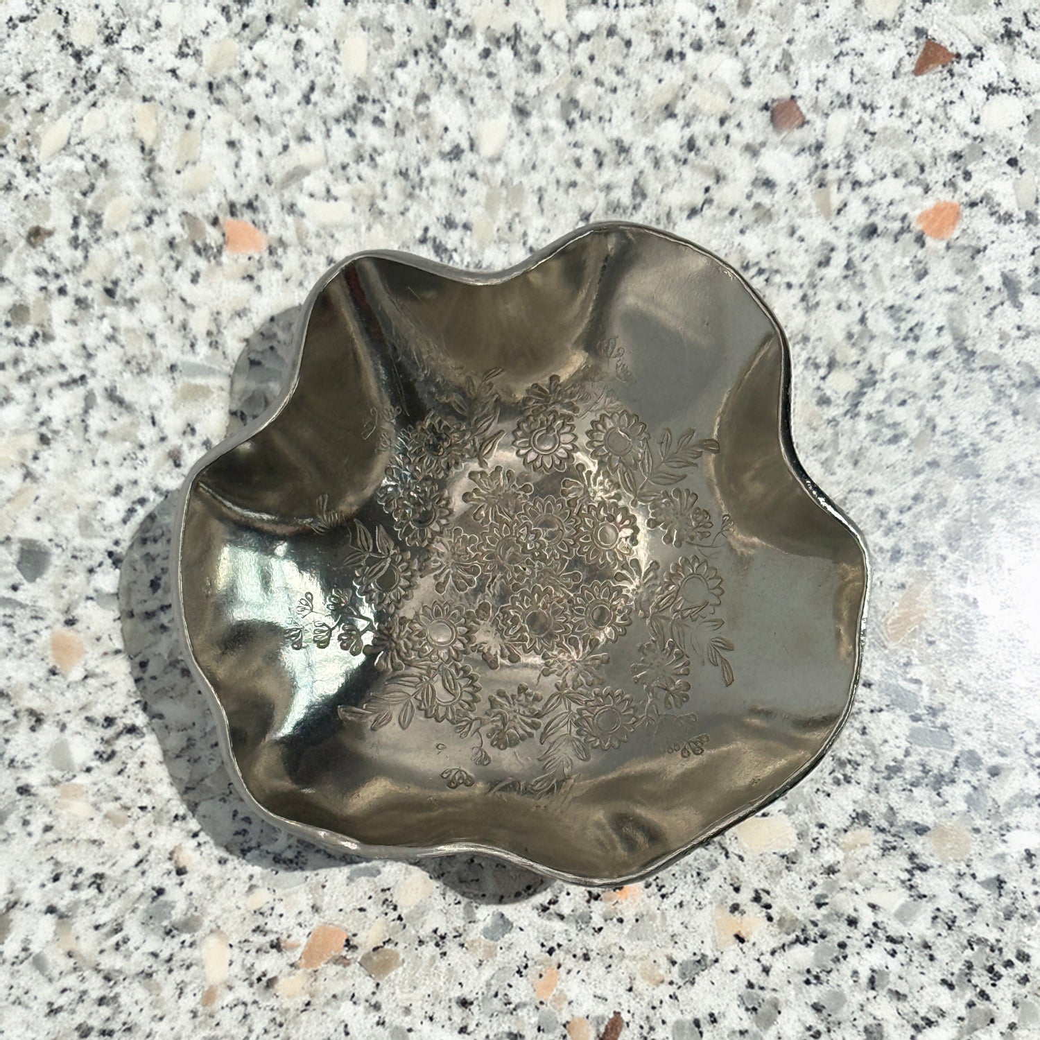 A trinket dish handmade from Cornish tin with waved edges and a hand stamped flower design in the base.