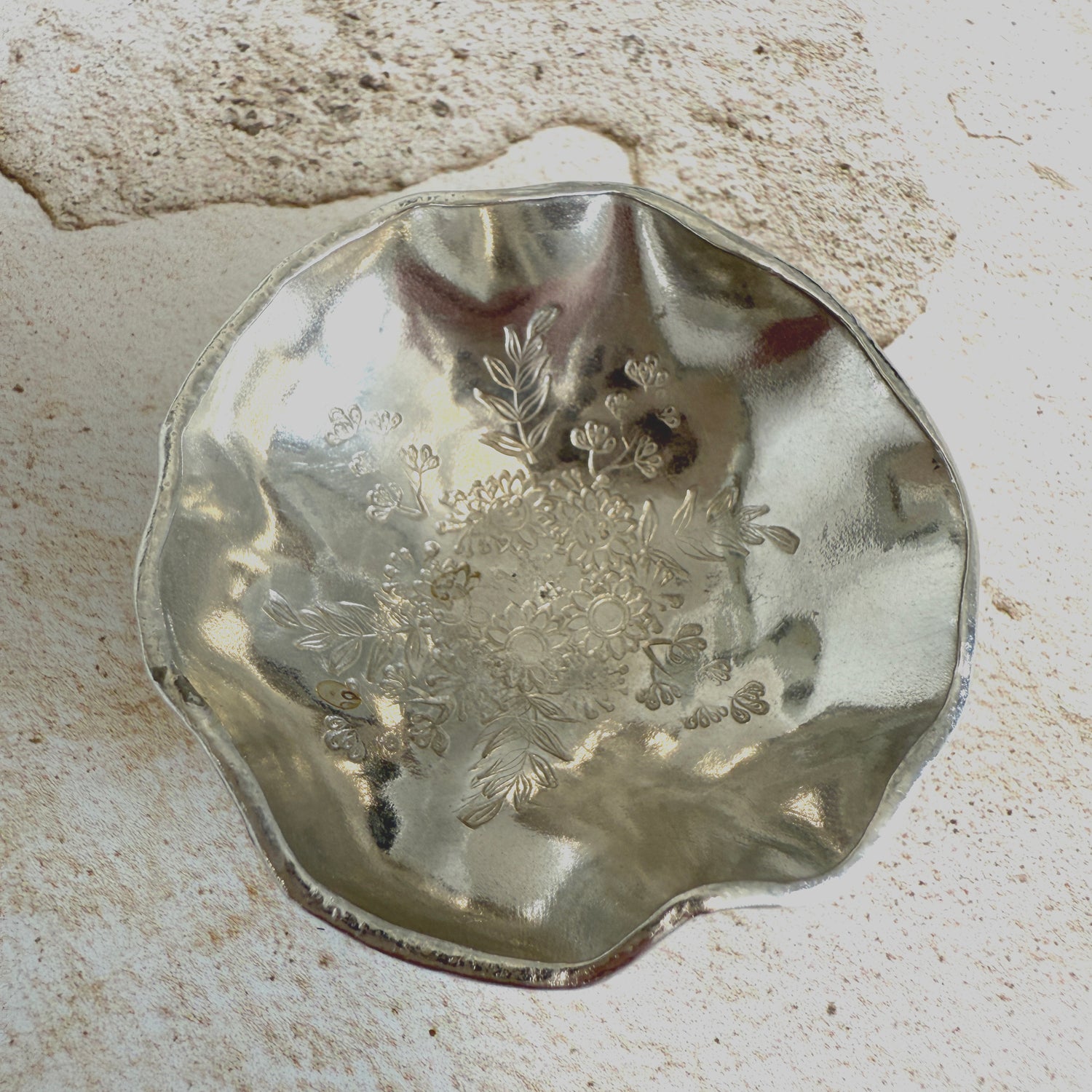 A trinket dish formed from Cornish tin with undulating edges and a stamped flower design